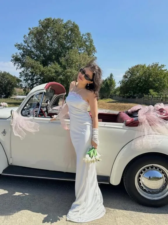 Beyaz gelinlikli gelin, tül ve pudra çiçeklerle süslenmiş krem cabrio Vosvos gelin arabası Royal'in yanında