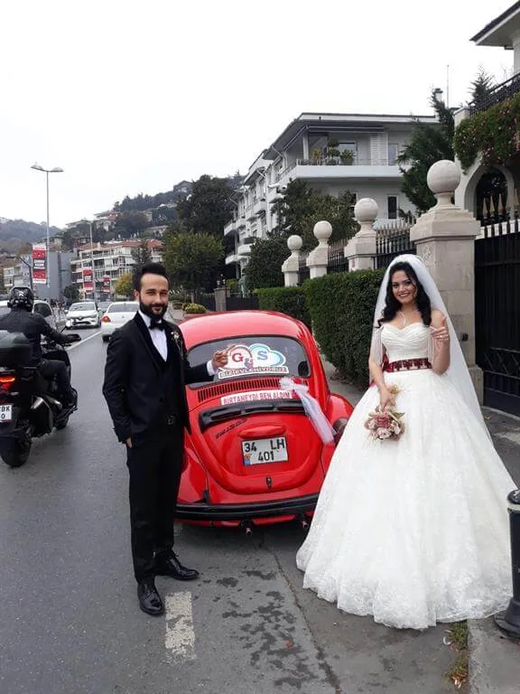 Beyaz gelinlikli gelin ve damat, tül süslemeli kırmızı standart kasa Vosvos gelin arabasının yanında