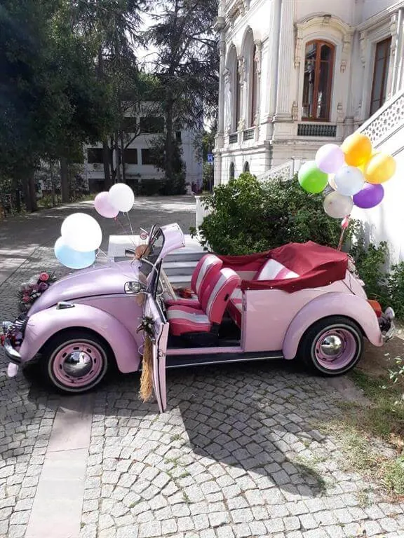 Kapıları açık, arkasında pastel balon demeti olan açık pembe cabrio Vosvos gelin arabası