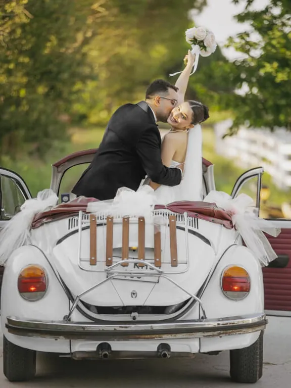 Beyaz tülle süslenmiş krem cabrio Vosvos gelin arabasında öpüşen gelin ve damat
